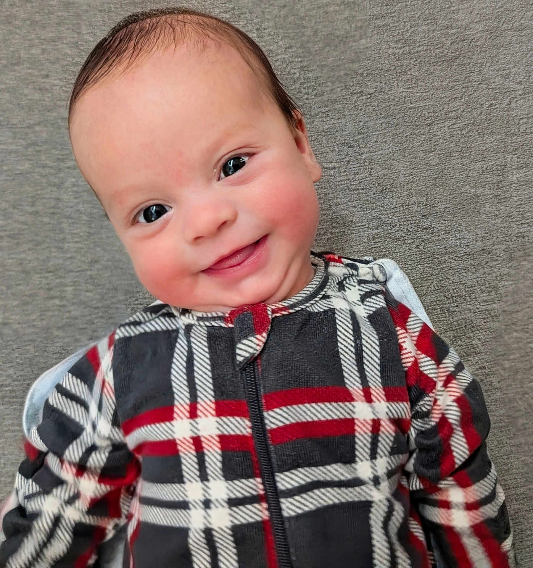 Quentin is registered to the contest to win money with this photo: baby, smiling, face, plaid, clothing, infant, child, cute, portrait, happy, cheeks, eyes, texture, fabric, zipper, cozy, lying_down, background, closeup, skin