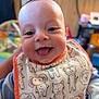 Quentin is registered to the contest to win money with this photo: baby, smiling, tongue_out, bib, animal_print, indoor, child, happy, cute, face, head, clothing, infant, person, portrait, closeup, cheerful, soft_light, seated, young_child