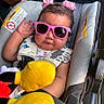 baby, child, infant, stroller, sunglasses, pink_sunglasses, flower_hair_clips, stuffed_toy, yellow_toy, seated, portrait, outdoor, vehicle, safety_harness, curly_hair, looking_at_camera, playful, colorful, baby_carriage, casual