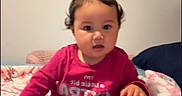 Adalina Lopez joined the competition — help win amazing prizes! baby, child, infant, sitting, bed, bedroom, floral_bedding, toy, green_toy, long_sleeves, pants, bare_feet, hair_bows, curious, indoors, portrait, face, smiling, furniture, social_media_screenshot