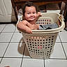 Adalina Lopez is registered to the contest to win money with this photo: baby, child, laundry_basket, clothes, indoors, tile_floor, wooden_furniture, smiling, portrait, sitting, infant, bare_shoulders, household, laundry, basket, happy, face, floor, home, photography