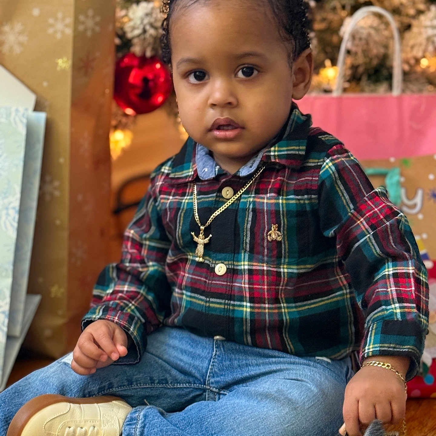 Eyden is registered to the contest to win money with this photo: bracelet, casual_clothing, child, christmas_tree, curly_hair, cute, decorations, festive, gift_bags, holiday, indoors, jeans, necklace, plaid_shirt, portrait, sitting, toddler, toy_car, wooden_floor, young_child