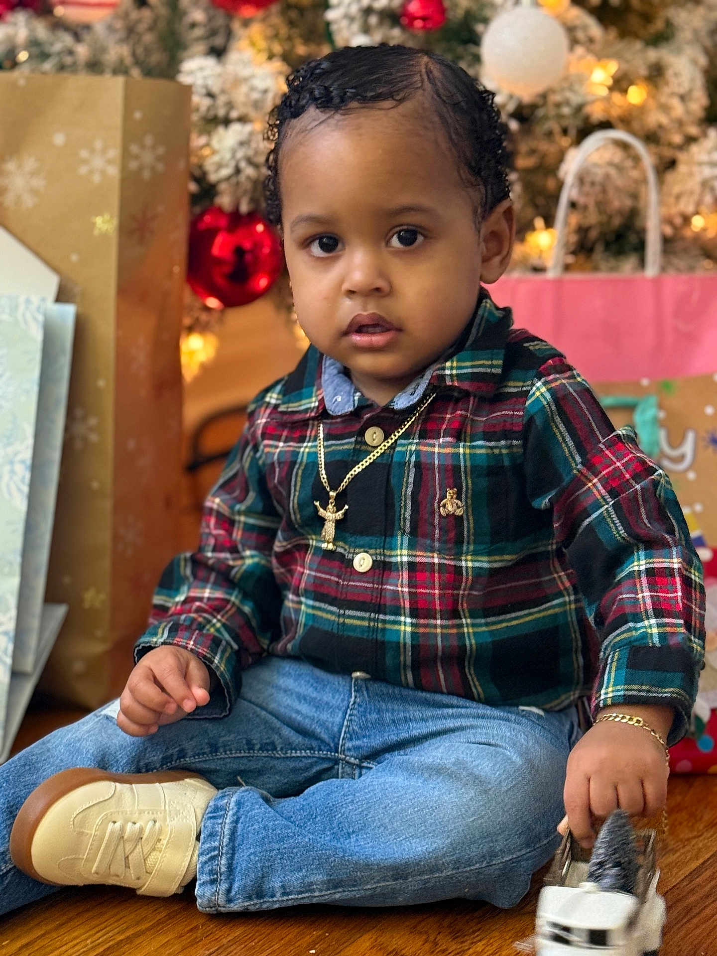 Eyden is registered to the contest to win money with this photo: toddler, child, plaid_shirt, jeans, toy_car, christmas_tree, holiday, gift_bags, wooden_floor, curly_hair, bracelet, necklace, indoors, festive, decorations, cute, portrait, sitting, young_child, casual_clothing