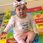 Charlee is registered to the contest to win money with this photo: baby, child, infant, headband, pink, shirt, text, play_mat, colorful, alphabet, animal, floor, sitting, barefoot, indoors, cute, expression, person, young, casual_clothing