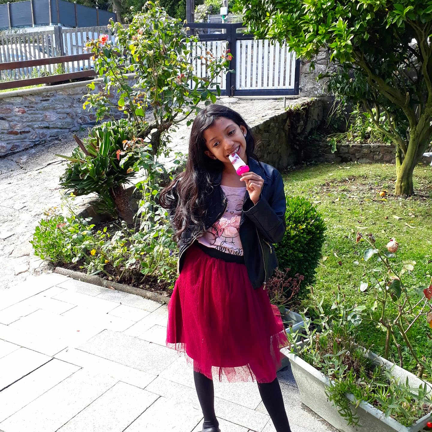Alina a rejoint le concours — aidez-le/la à gagner de superbes lots ! black_jacket, black_shoes, black_tights, child, daylight, garden, girl, greenery, happy, nature, outdoor, plant, playful, popsicle, portrait, red_skirt, sidewalk, smile, sunlight, tree