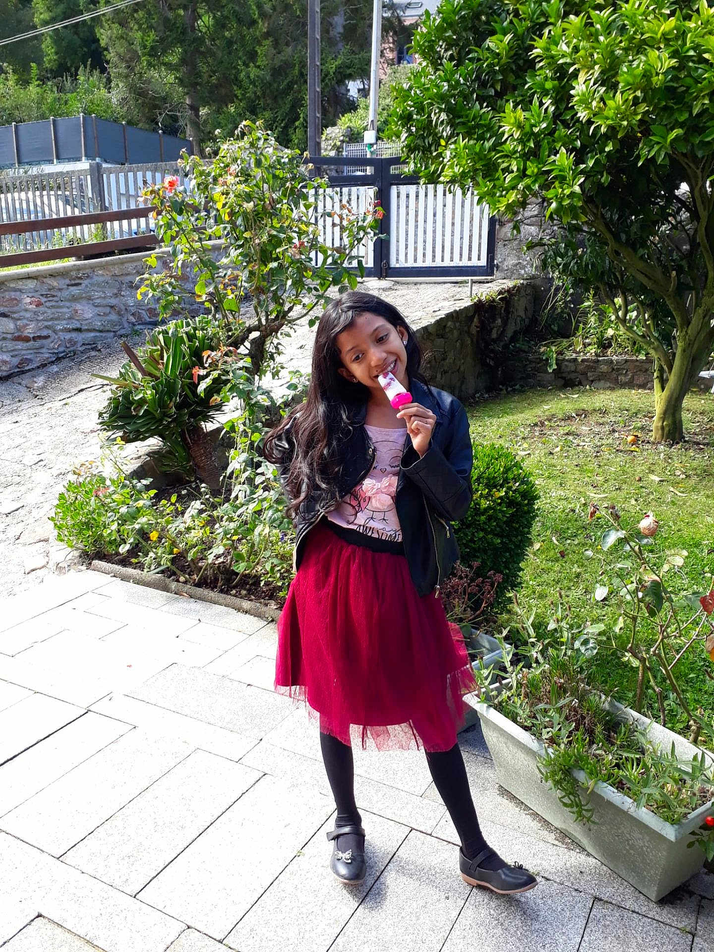Alina a rejoint le concours — aidez-le/la à gagner de superbes lots ! child, girl, outdoor, garden, plant, tree, popsicle, smile, black_jacket, red_skirt, black_tights, black_shoes, sidewalk, sunlight, greenery, happy, playful, nature, portrait, daylight