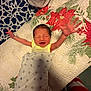 newborn, baby, infant, smile, arms_stretched, blanket, polka_dot, quilt, holiday_theme, red, green, yellow_clothing, happy, lying_down, hand, bed, fabric, pattern, indoors, person