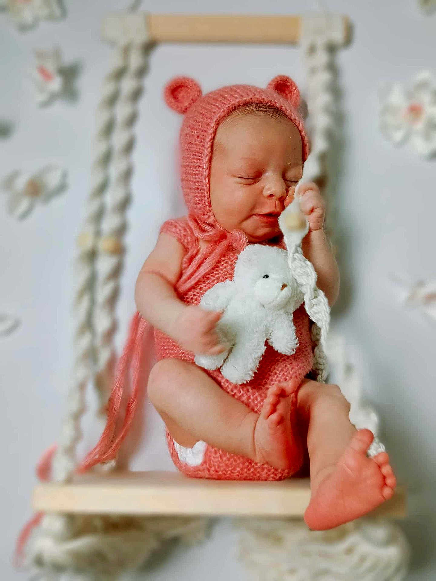 Tanirth is registered to the contest to win money with this photo: newborn, baby, pink_clothing, knitted_hat, teddy_bear, swing, sleeping, infant, cute, soft_lighting, indoor, portrait, baby_feet, baby_hands, cozy, decorations, wooden_swing, peaceful, child, adorable