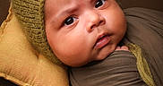 Rihan joined the competition — help win amazing prizes! baby, bonnet, brown, child, closeup, curious, expression, face, headwear, indoors, infant, mustard_yellow, newborn, olive_green, pillow, portrait, skin, soft_texture, swaddle, wrapped