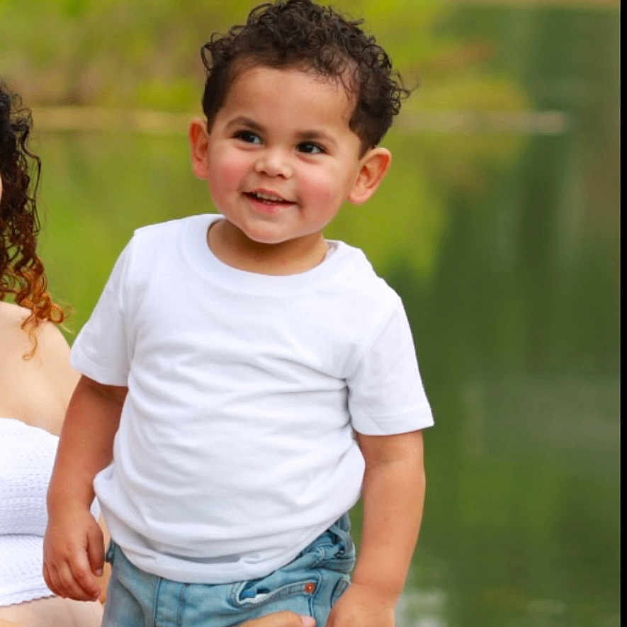 Miles joined the competition — help win amazing prizes! adult_hand, casual_clothing, child, curly_hair, daylight, grass, greenery, happy, jeans, lake, nature, outdoor, person, portrait, smiling, supporting_hand, tattoo, toddler, white_tshirt, young_child