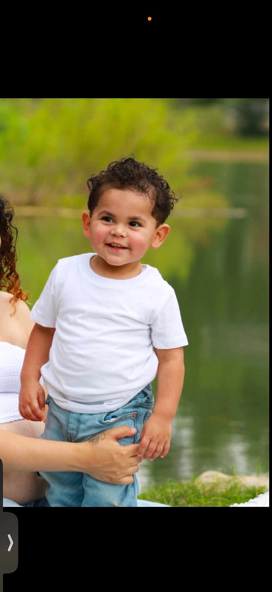 Miles joined the competition — help win amazing prizes! toddler, child, curly_hair, white_tshirt, jeans, smiling, outdoor, lake, greenery, adult_hand, tattoo, nature, grass, person, portrait, happy, young_child, casual_clothing, daylight, supporting_hand