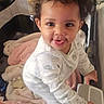 Jasmine is registered to the contest to win money with this photo: baby, child, playpen, blanket, smile, face, curly_hair, indoors, infant, clothing, toy, hand, pink_blanket, white_pajamas, person, happy, standing, home, cute, expression