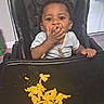 baby, child, high_chair, food, macaroni, cheese, messy, indoor, person, feeding, clothing, face, hand, tray, seat, black, happy, cute, young, infant