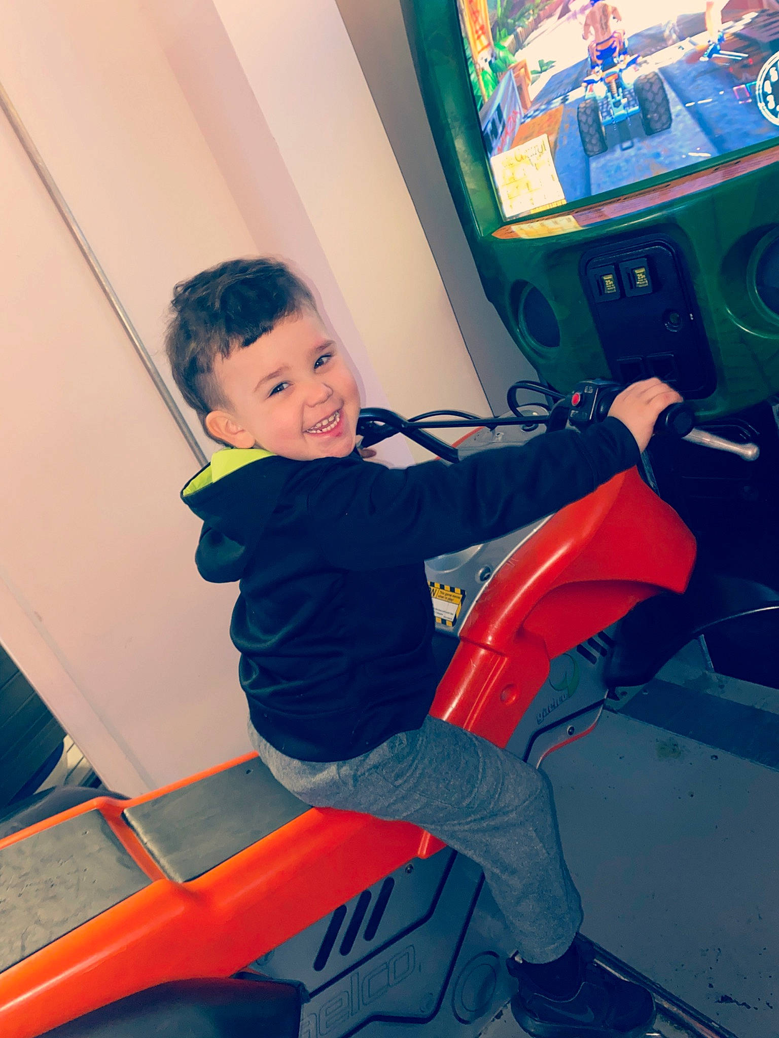 Adan is registered to the contest to win money with this photo: arcade_game, child, elbow, electric_blue, fun, human_leg, joy, knee, leisure, machine, person, recreation, room, shoulder, sitting, smile, sneakers, sportswear, t_shirt, thigh