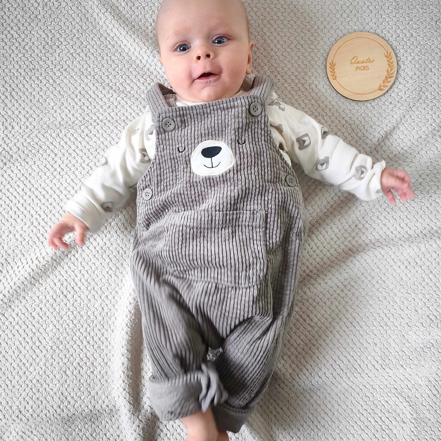 Armand a rejoint le concours — aidez-le/la à gagner de superbes lots ! baby, bear_face, child, clothing, corduroy_overalls, curious, cute, feet, hands, indoor, infant, lying_down, milestone_marker, pattern, plaid_blanket, portrait, smiling, soft_lighting, texture, wooden_plaque