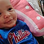 baby, blanket, blue_jersey, child, closeup, clothing, cozy, face, head, indoor, infant, person, phillies, pillow, pink, polka_dot, portrait, resting, smiling, soft