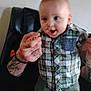 Andrew is registered to the contest to win money with this photo: baby, black_chair, blue_shoes, blurred_face, casual_clothing, child, excited, footwear, green_shorts, holding_hands, home, indoor, person, plaid_shirt, smiling, support, tattooed_hands, toddler, walking, young_child