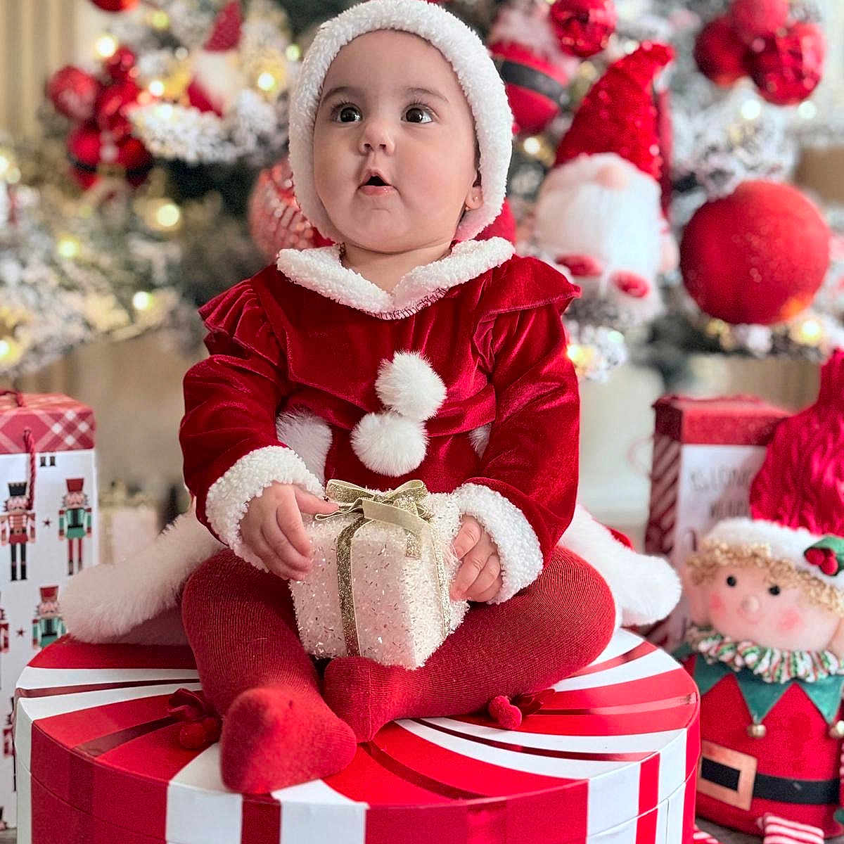 Camelia is registered to the contest to win money with this photo: baby, child, christmas, cute, decorations, doll, festive, floor, gift, hat, holiday, indoor, ornaments, present, red_clothing, seasonal, sitting, smiling, toy, tree