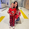 woman, child, baby, red_clothing, pajamas, smiling, pacifier, indoor, hallway, floor_tiles, plaid_pants, holding, family, portrait, happy, casual, kneeled, long_hair, cute, holiday
