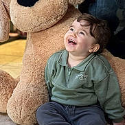 Noah a rejoint le concours — aidez-le/la à gagner de superbes lots ! child, toddler, smiling, laughing, stuffed_animal, plush_dog, large_toy, indoor, tile_floor, green_sweatshirt, casual_clothing, portrait, candid, sitting, happy, baby_teeth, cozy, soft_texture, playtime, gaze_up