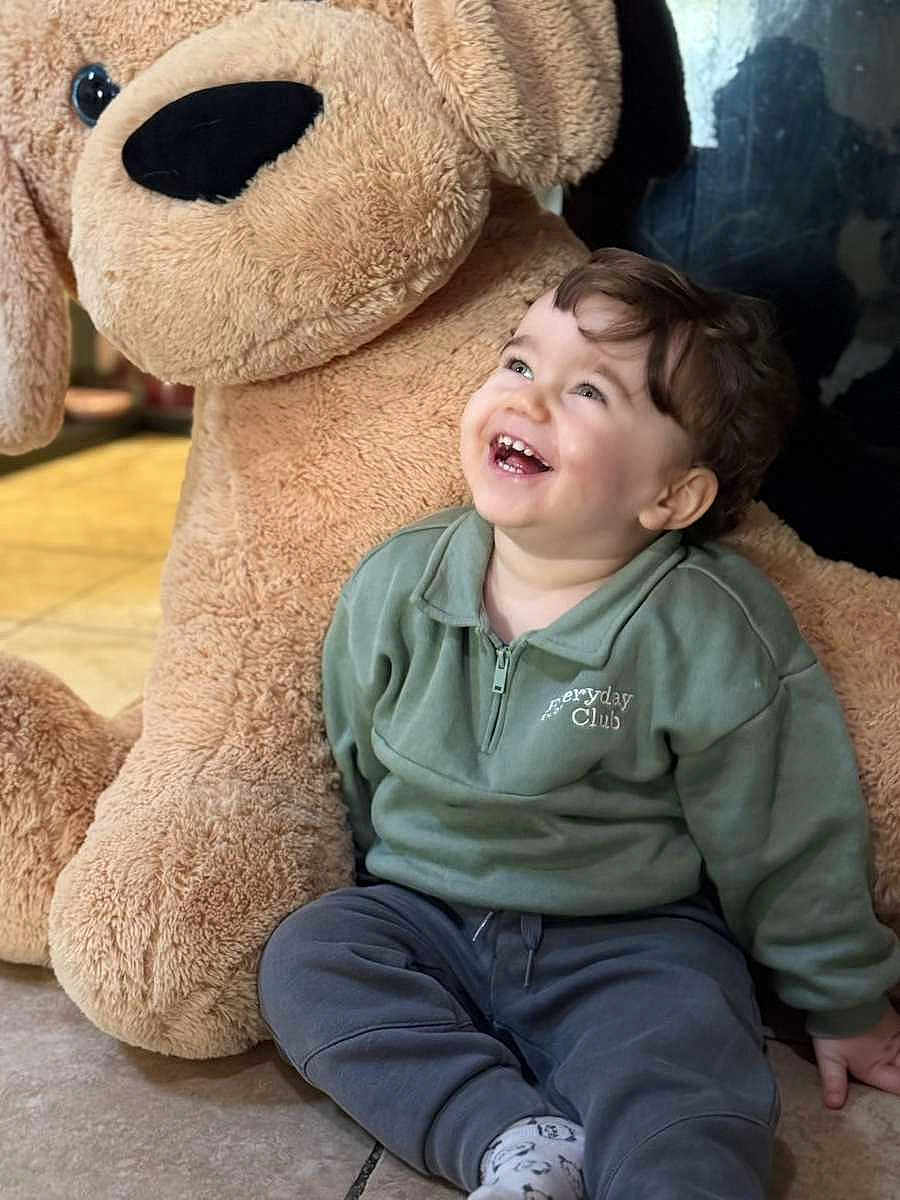 Noah a rejoint le concours — aidez-le/la à gagner de superbes lots ! child, toddler, smiling, laughing, stuffed_animal, plush_dog, large_toy, indoor, tile_floor, green_sweatshirt, casual_clothing, portrait, candid, sitting, happy, baby_teeth, cozy, soft_texture, playtime, gaze_up
