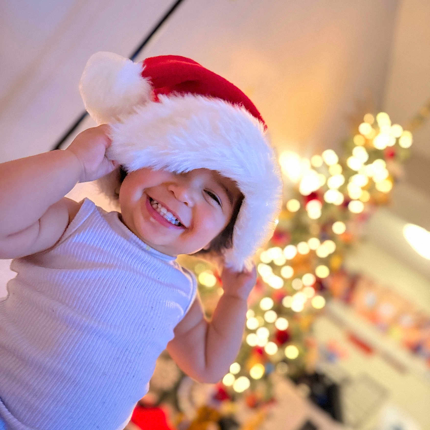Lusiana joined the competition — help win amazing prizes! blurred_background, cheerful, child, christmas, cute, decorations, face, festive, festivity, happy, holiday, holiday_spirit, indoors, joy, lights, portrait, santa_hat, smiling, toddler, white_tank_top