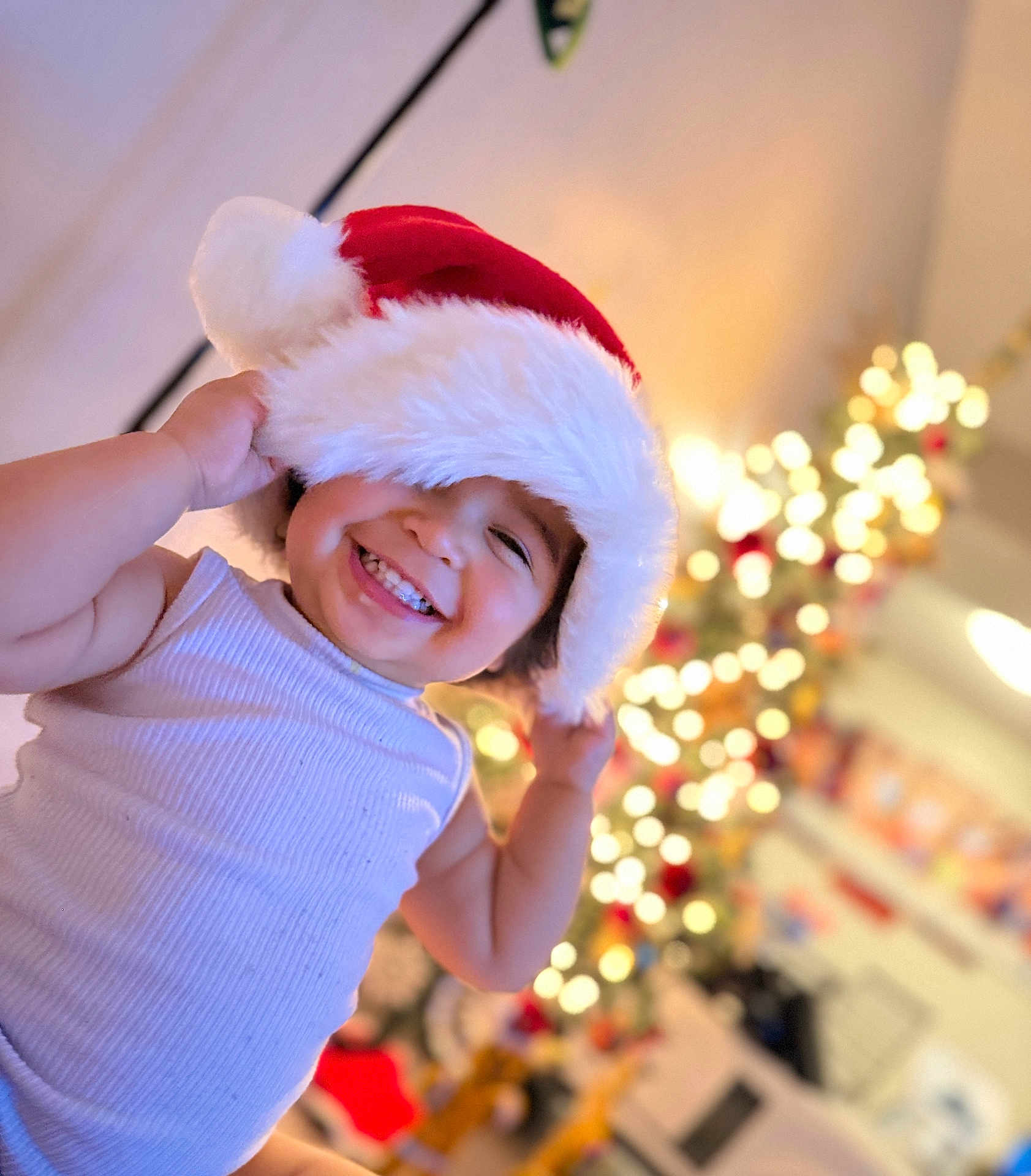 Lusiana joined the competition — help win amazing prizes! child, toddler, smiling, santa_hat, christmas, holiday, festive, indoors, happy, portrait, cute, white_tank_top, lights, decorations, blurred_background, holiday_spirit, cheerful, festivity, face, joy