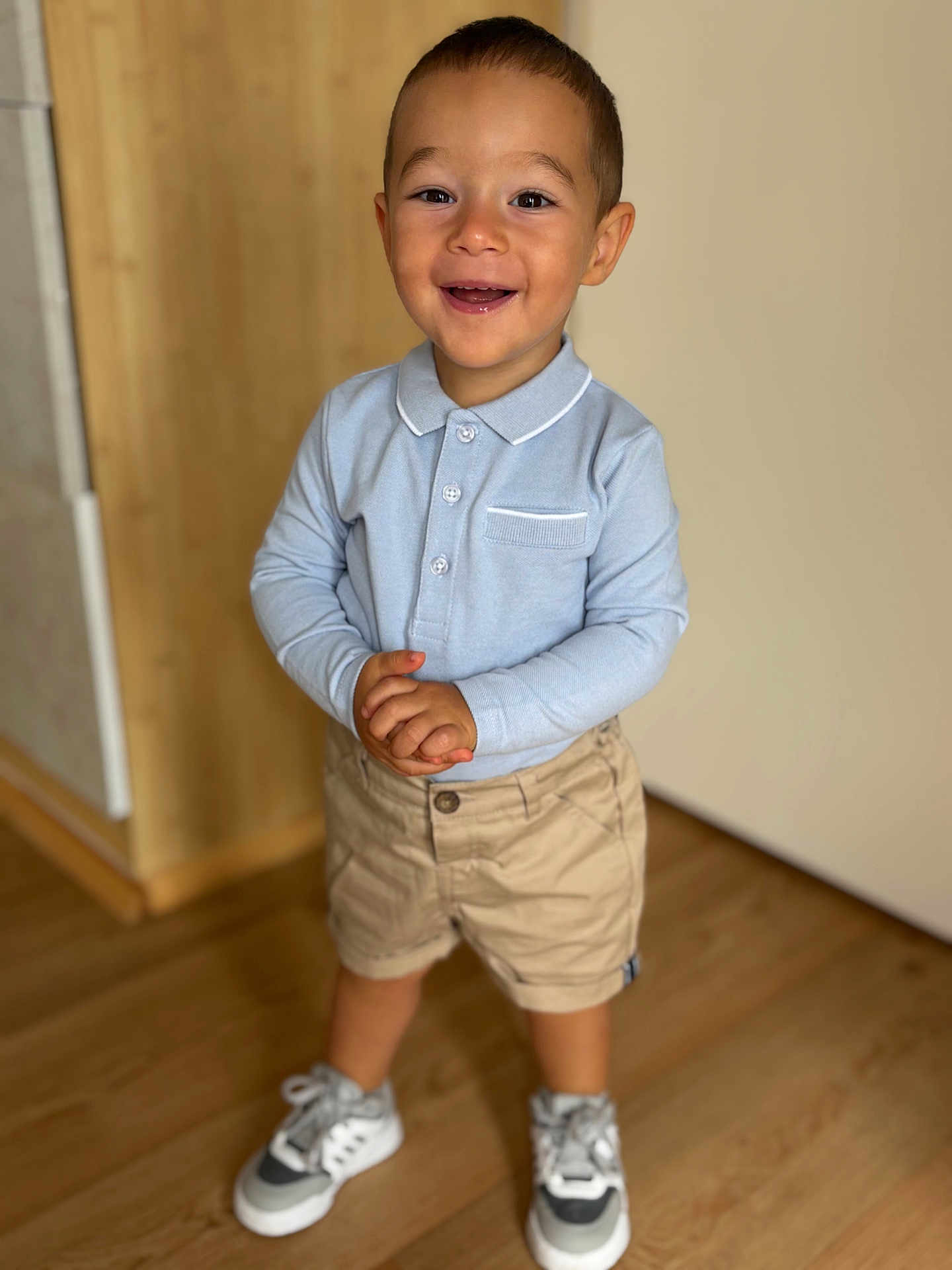 Nayan a rejoint le concours — aidez-le/la à gagner de superbes lots ! toddler, smiling, child, indoor, standing, casual_clothing, shorts, polo_shirt, sneakers, wooden_floor, happy, portrait, young_child, playful, cute, person, real_photo, light_blue, beige, short_hair