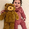 baby, big_eyes, blanket, chubby_cheeks, close_up, cute, hair, happy, indoor, infant, lying_down, onesie, pink_clothing, plush_toy, portrait, smiling, soft_texture, stuffed_animal, teddy_bear, toddler