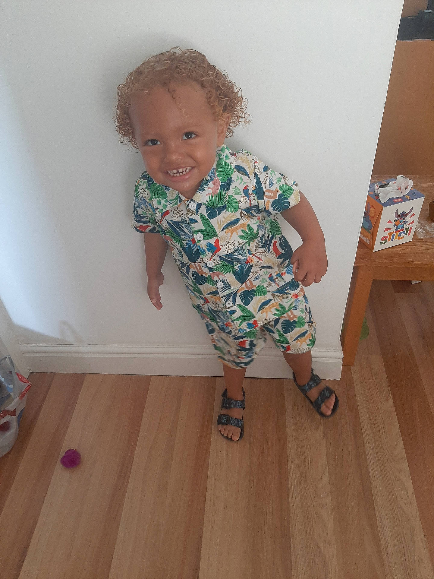 Mateus joined the competition — help win amazing prizes! casual, child, colorful_clothing, curly_hair, cute, flooring, happy, home, indoor, person, playful, portrait, sandals, smiling, standing, toddler, tropical_pattern, white_wall, wooden_floor, young_child