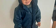 Mateus joined the competition — help win amazing prizes! boots, casual, child, clothing, curly_hair, cute, flooring, happy, hood, indoor, pacifier, person, portrait, raincoat, smile, standing, toddler, white_wall, wooden_floor, young_child
