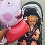 Mateus is registered to the contest to win money with this photo: balloon, child, clothing, curly_hair, daylight, hand, happy, outdoor, pacifier, pavement, peppa_pig, person, seatbelt, sidewalk, smiling, stroller, toddler, toy, urban, vehicle