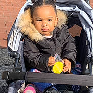 Bradlee is registered to the contest to win money with this photo: toddler, child, stroller, jacket, fur_hood, outdoor, sunlight, pink_bottle, shoes, hair_buns, serious_expression, clothing, person, seat, toy, pavement, daylight, small_hands, cute, bundle_up