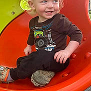Axel is registered to the contest to win money with this photo: toddler, child, playground, slide, orange, curly_hair, blonde, smiling, happy, casual_clothing, sneakers, outdoor, play, fun, park, young_child, sitting, toy_design, daylight, cute