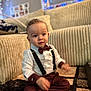 baby, big_eyes, bow_tie, carpet, child, couch, cozy, curly_hair, cute, decorations, formal_outfit, indoor, living_room, maroon_pants, portrait, sitting, smiling, suspenders, toddler, white_shirt