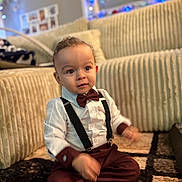 Jules a rejoint le concours — aidez-le/la à gagner de superbes lots ! baby, big_eyes, bow_tie, carpet, child, couch, cozy, curly_hair, cute, decorations, formal_outfit, indoor, living_room, maroon_pants, portrait, sitting, smiling, suspenders, toddler, white_shirt