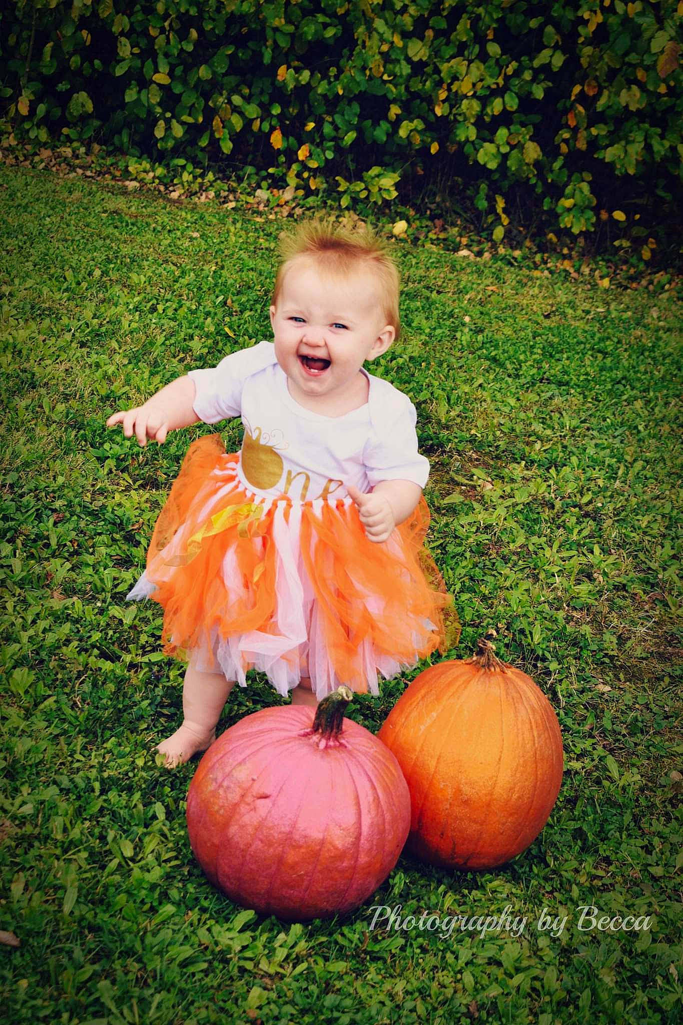 Olivia joined the competition — help win amazing prizes! baby_toddler_clothing, botany, calabaza, dress, eye, face, facial_expression, grass, happy, head, human_body, joy, leaf, orange, people_in_nature, person, plant, pumpkin, smile, squash