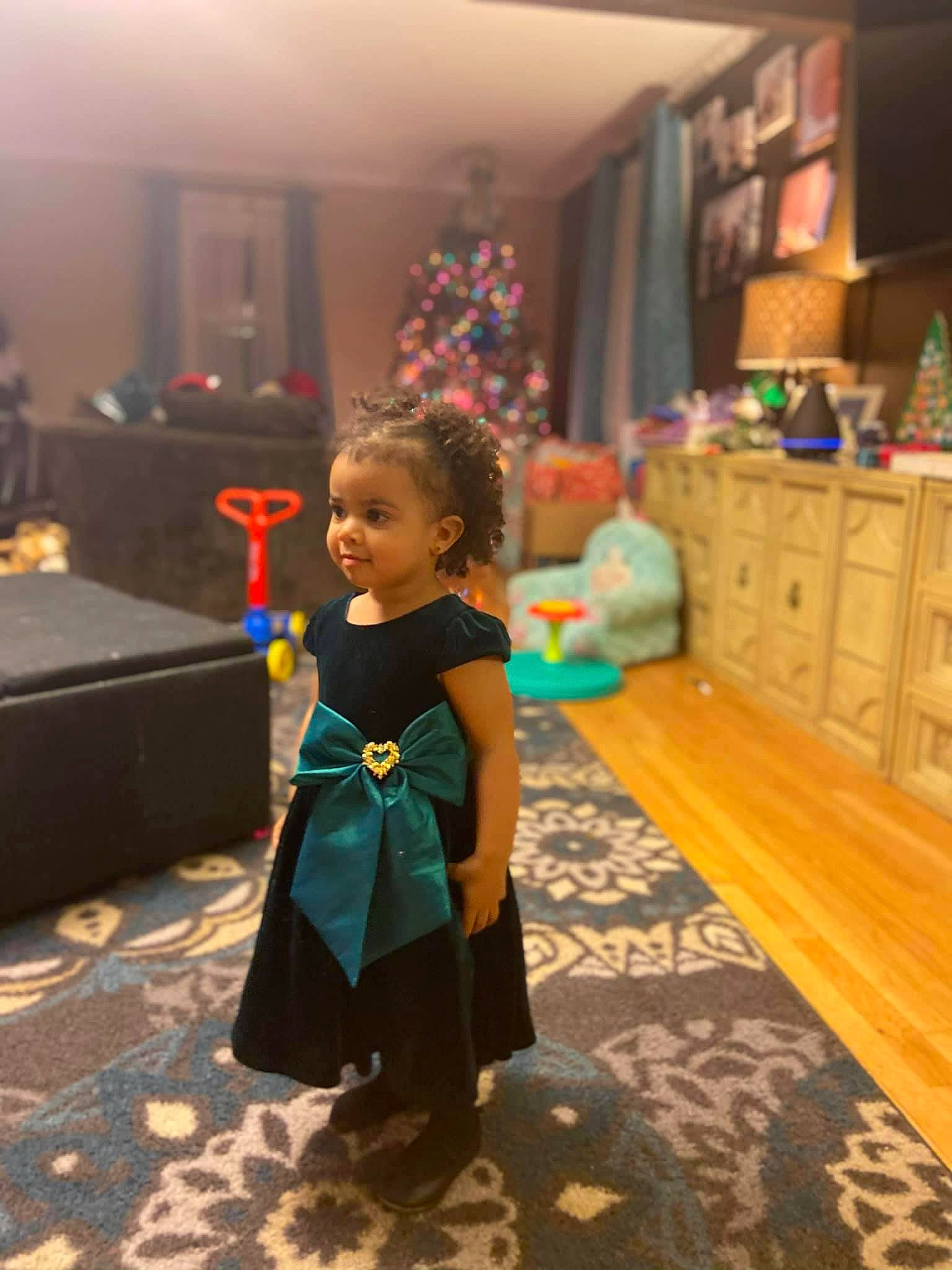 Layla is registered to the contest to win money with this photo: chest_of_drawers, child, christmas_tree, drawer, event, fashion_design, floor, flooring, formal_wear, fun, happy, human_body, leisure, living_room, person, play, room, sitting, suit, toddler