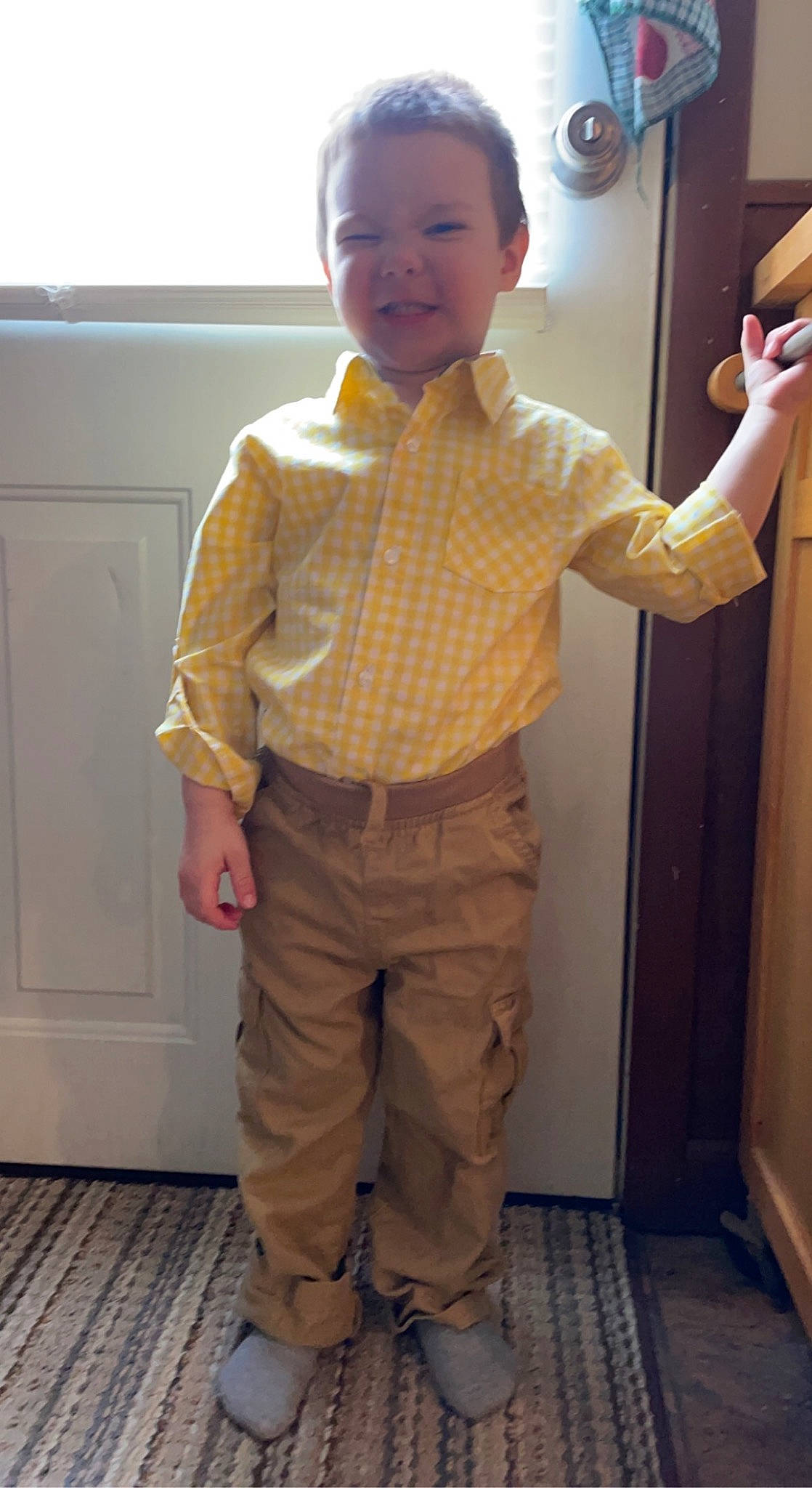 Konnor is registered to the contest to win money with this photo: arm, baby_toddler_clothing, door, dress_shirt, facial_expression, finger, gesture, hair, hand, head, human_body, joint, joy, khaki_pants, nose, person, shoulder, sleeve, smile, standing