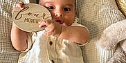 Isaiah joined the competition — help win amazing prizes! baby, infant, child, four_months, holding_sign, white_shirt, green_pants, plush_toy, blanket, soft_texture, curious_eyes, lying_down, wooden_sign, indoor, portrait, cute, small_hands, buttoned_shirt, baby_clothes, resting
