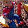 toddler, child, playground, denim_overalls, red_shirt, red_crocs, yellow_seat, wood_chips, outdoor, smiling, sitting, person, play_equipment, sunlight, happy, casual_clothing, young_child, daylight, cute, blue_eyes