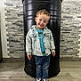 Lucas a rejoint le concours — aidez-le/la à gagner de superbes lots ! child, smiling, standing, denim_jacket, jeans, sneakers, indoor, flooring, brick_wall, black_cylinder, happy, portrait, casual_clothing, curly_hair, tshirt, fashion, person, cute, kid, playful
