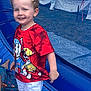 Lucas participe au concours pour gagner de l'argent avec cette photo : child, curly_hair, red_shirt, white_shorts, socks, inflatable, outdoor, smiling, tent, mesh, event, playful, young_child, standing, blue_surface, daylight, cute, fun, happy, casual_clothing