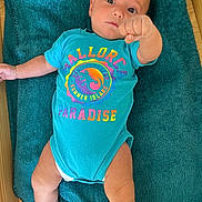 Elyo participe au concours pour gagner de l'argent avec cette photo : baby, infant, onesie, towel, floor, wooden_floor, person, child, cute, colorful_clothing, blue, lying_down, hand, arm, leg, face, eyes, expression, indoor, playful