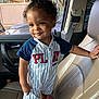 Tyrion Jr is registered to the contest to win money with this photo: toddler, child, car_interior, seat, toy_dinosaur, smile, curly_hair, clothing, shorts, sneakers, window, door_handle, seatbelt, sunlight, hand, face, person, playful, indoor, portrait