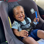 Tyrion Jr is registered to the contest to win money with this photo: toddler, car_seat, child, smiling, sunglasses, blue_shorts, shirt, seatbelt, car_interior, sunlight, happy, holding_object, infant, sitting, cute, young_child, seat, safety_harness, toy, relaxed