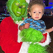 Weston joined the competition — help win amazing prizes! child, person, grinch, costume, santa_suit, green_mask, green_fur, holiday_lights, night, outdoor, holding, curly_hair, blue_shirt, camouflage_pattern, festive, christmas, portrait, face, expression, event