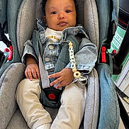 Nelson a rejoint le concours — aidez-le/la à gagner de superbes lots ! baby, infant, car_seat, denim_jacket, pacifier, pacifier_clip, child, clothing, seatbelt, face, hand, footwear, socks, person, indoor, shopping, store, curly_hair, cute, sitting