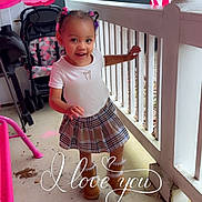 Julianna is registered to the contest to win money with this photo: toddler, child, porch, smiling, plaid_skirt, boots, white_tshirt, hair_buns, stroller, car, railing, outdoor, concrete_floor, pink, love_text, happy, cute, playful, daylight, person