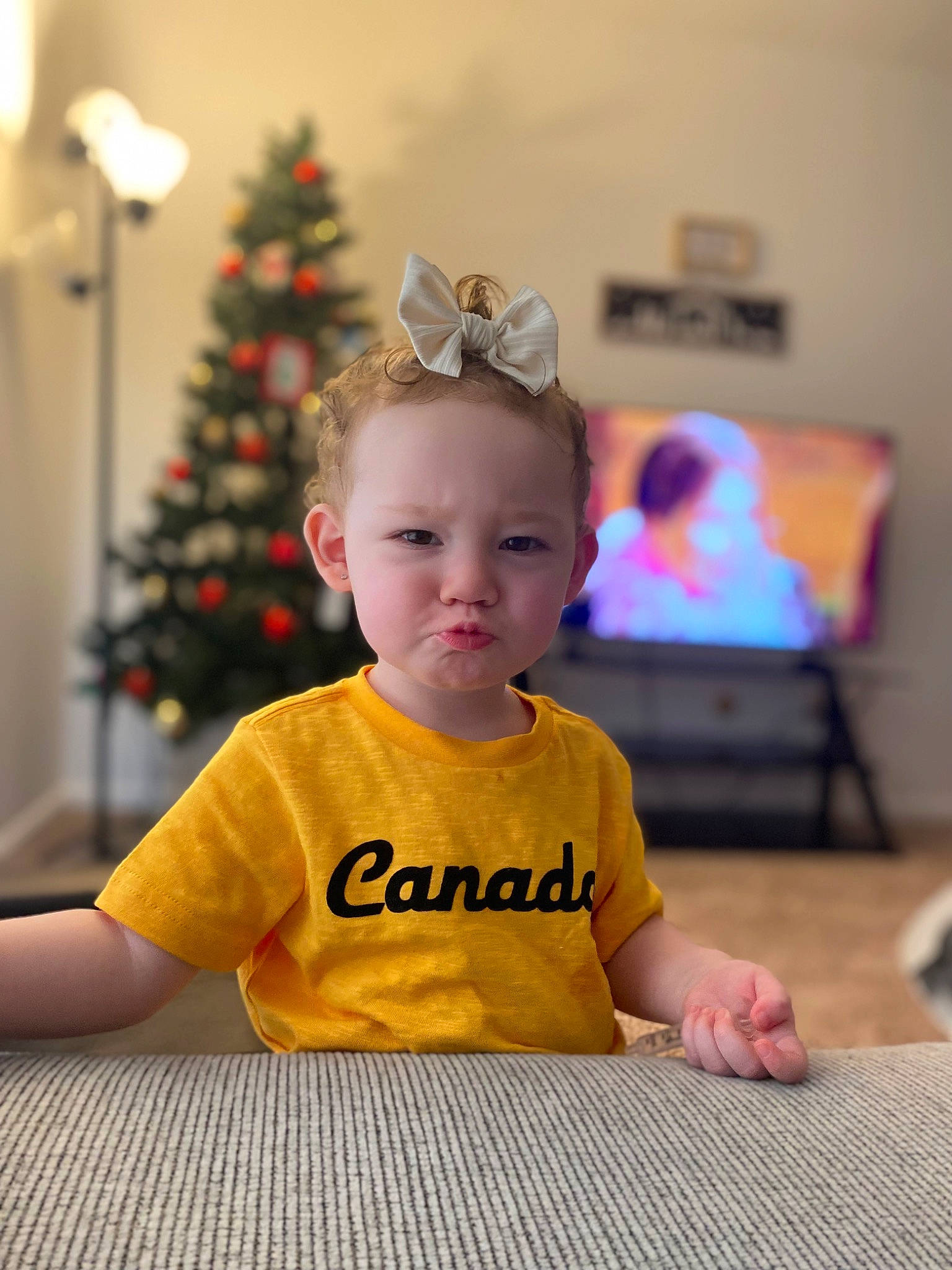 Nala is registered to the contest to win money with this photo: baby, baby_toddler_clothing, child, christmas, christmas_eve, christmas_ornament, christmas_tree, event, facial_expression, fashion_accessory, flooring, fun, happy, holiday, ornament, person, room, sitting, standing, t_shirt